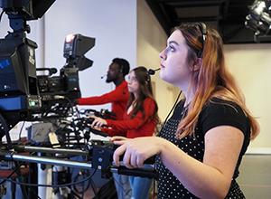 Communication student running camera in the news room on campus.